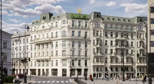 Elegancki budynek z logo Rolex na dachu, symbolizujący nowy świat w Warszawie. Ulica tętni życiem, ludzie spacerują, a samochody przejeżdżają.