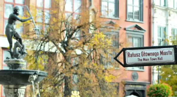 Fontanna Neptuna i drogowskaz na Ratusz Głównego Miasta w altstadt Danzig. Jesienne liście drzew tworzą tło dla zabytkowej architektury.