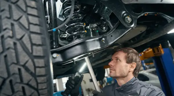 Mechanik bada zawieszenie w samochodzie, oświetlając je latarką. Widać sprężynę i amortyzator.