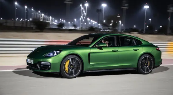 Zielony Porsche Panamera GTS pędzi nocą po torze wyścigowym, oświetlonym jaskrawymi światłami.