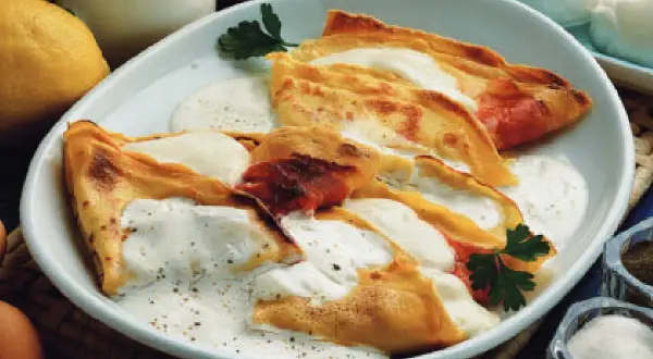 Crepes ripiene di prosciutto e formaggio, condite con una salsa cremosa. Una deliziosa panna acida ricetta per un piatto unico.