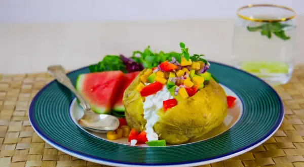 En saftig bakad potatis med en färgglad fyllning av grönsaker och en klick krämig ost. Serveras med vattenmelon och en frisk dryck.