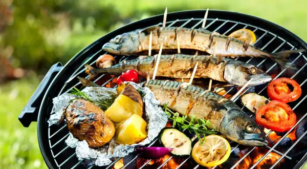 Drei ganze Makrelen werden auf einem Grill mit Kartoffeln, Tomaten und Zucchini gegrillt.