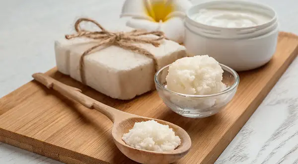 Jabón artesanal, crema y exfoliante de **grasa de karité** en cuchara de madera, sobre tabla de bambú.