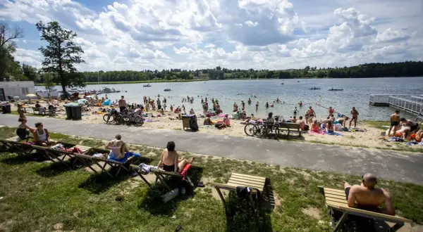 Tłum ludzi odpoczywa nad jeziorem w Poznaniu, opalając się na plaży i kąpiąc w wodzie.