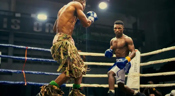 Two boxers face off in a ring, one in camouflage shorts, the other in blue. Their boxing opponent is ready for the fight.