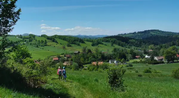 Dwie dziewczynki wędrujące po zielonych wzgórzach Gór Sowich z widokiem na wieś.