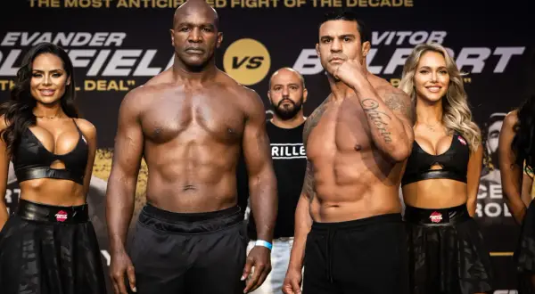 Evander Holyfield och Vitor Belfort står redo för en episk match. Ringflickor flankerar de muskulösa boxarna.