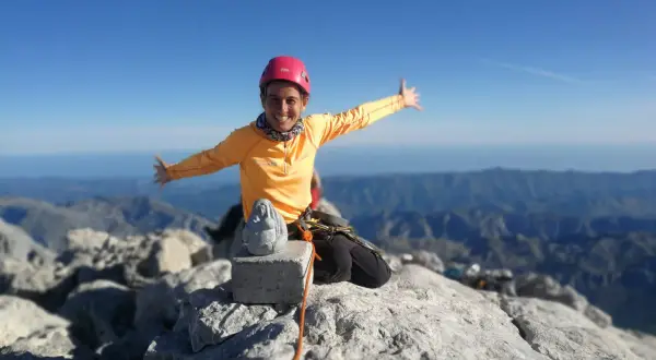Szczęśliwa alpinistka na szczycie góry, z widokiem na pasmo górskie. W tle widać morze. To szczyt Naranjo de Bulnes.