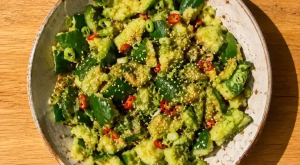 En skål med krossad gurka sallad, toppad med sesamfrön, chili och salladslök. En härlig och fräsch rätt.