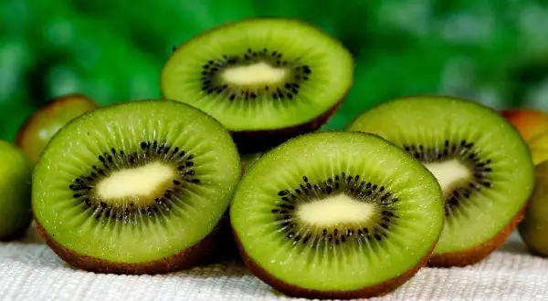 Kilka przekrojonych owoców kiwi z widocznymi czarnymi pestkami na jasnym tle.