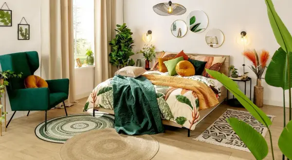 Sypialnia boho inspiracje: łóżko z pościelą w liście, zielony fotel, dywany i rośliny tworzą przytulną atmosferę.