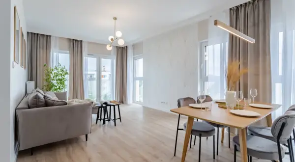 Nowoczesny salon z jadalnią. Szara kanapa, drewniany stół z krzesłami, ozdobna ściana i okna. Kto to? Flipper, bo tak nazywa się ten styl.