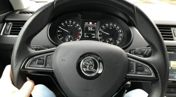 Blick auf das Lenkrad eines Autos mit Tachometeranzeige 55 km/h. Die Spurstange einstellen ist hier nicht direkt sichtbar, aber die Fahrt geht weiter.