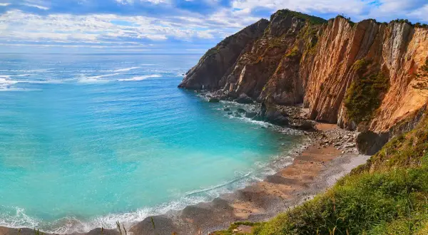 Aguas turquesas bañan la **cascada playa del Silencio**, rodeada de imponentes acantilados ocres y vegetación exuberante.