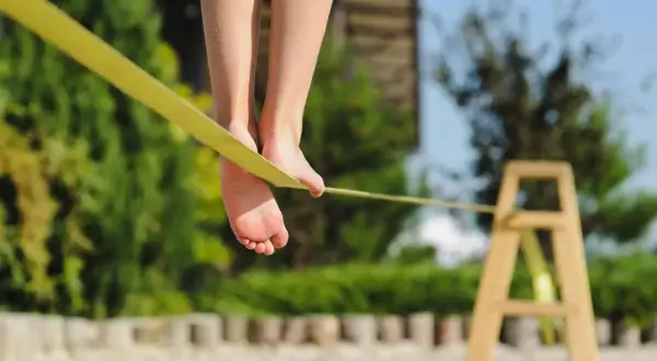 Füße balancieren auf einer gelben Slackline, die an einem Holzgestell befestigt ist.