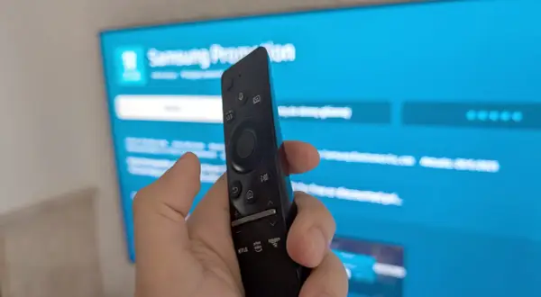 Pilot do telewizora Samsung w dłoni, ekran pokazuje menu, jak ściągnąć aplikacje na TV Samsung.