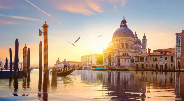 Gondola naviga sul Canal Grande al tramonto, con la maestosa Basilica di Santa Maria della Salute che domina lo skyline.