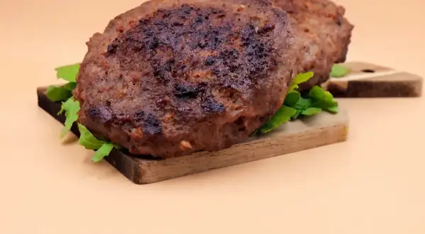 Dwa soczyste kotlety z wołowiny, idealne do burgerów, leżą na desce z rukolą. Prosty przepis na to, jak zrobić kotlety z wołowiny.