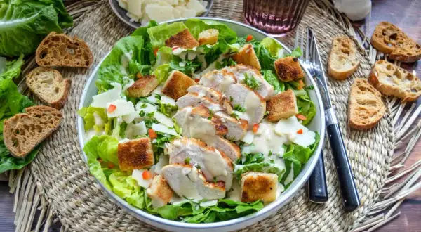 Ein köstlicher Cesar Salat mit gegrilltem Hähnchen, Croutons und cremigem Dressing. Dazu passen geröstete Brotscheiben.