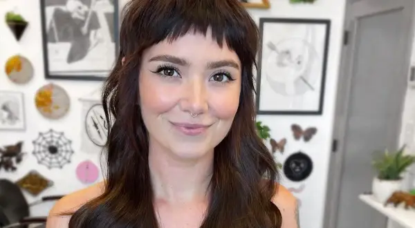 Uśmiechnięta kobieta z ciemnymi włosami i odważnymi baby bangs.