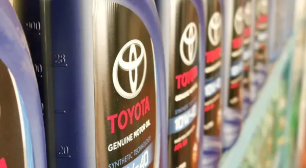 Rząd butelek oryginalnego oleju Toyota. Kto produkuje? Toyota, znana marka samochodów, produkuje również wysokiej jakości oleje silnikowe.