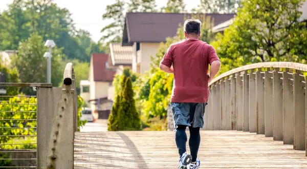 Un homme court sur un pont en bois, profitant du soleil matinal. C'est le meilleur moment pour courir, avec l'air frais et la nature verdoyante.