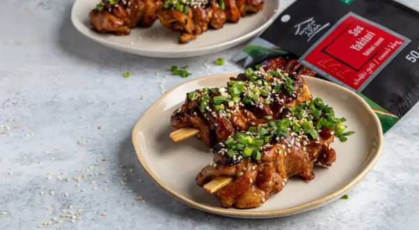 Pyszne yakitori na patyczkach, polane sosem i posypane sezamem i szczypiorkiem. Obok opakowanie sosu Yakitori.