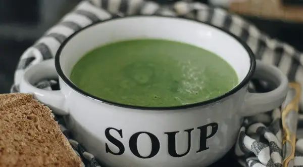 Zielony kremowy zupa w misce z napisem "SOUP". Idealna do mrożenia zup, by cieszyć się smakiem przez cały rok. Obok kromka chleba.