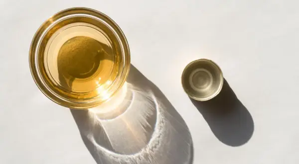 Ein Glas mit goldenem Apfelessig steht neben seinem Deckel. Sonnenschein wirft interessante Schatten. Bereit, Apfelessig zu trinken.