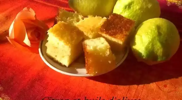 Gâteau au citron et à l'huile d'olive, une recette gâteau simple et délicieuse. Des parts de gâteau moelleux côtoient des citrons frais et une rose orangée sur un fond rouge.