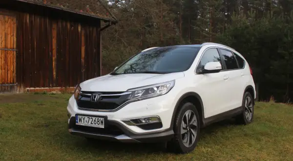 Biały Honda CR-V 2.0 benzyna zaparkowany na trawie obok drewnianej stodoły.