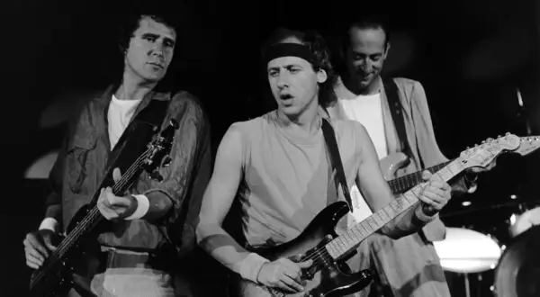 Trzech członków Dire Straits gra na gitarach podczas koncertu.