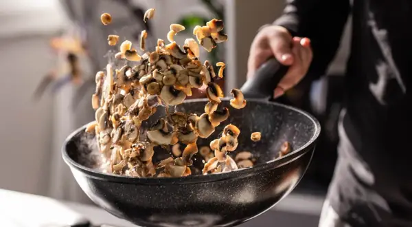 Man salteando champiñones en una sartén, mostrando cómo cocinar las setas para un plato delicioso.