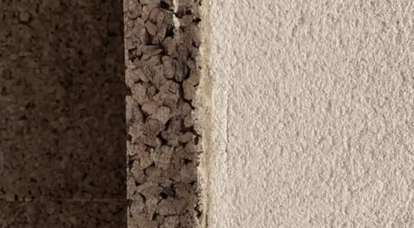 Dettaglio di un muro con strato di intonaco con sughero grezzo e finitura chiara e ruvida.