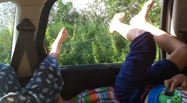 Dzieci odpoczywają, wyciągając nogi przez okno samochodu. Wygodne spanie w samochodzie podczas podróży.
