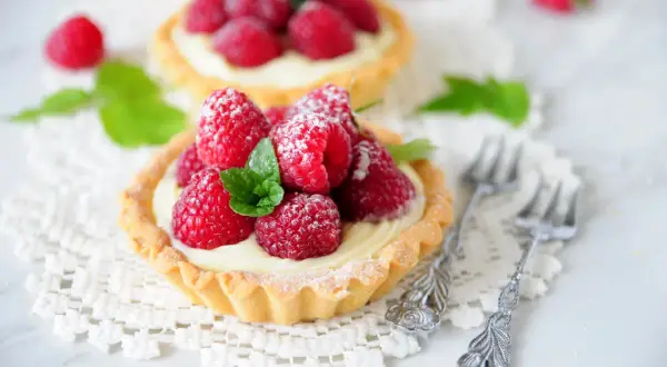 Malinowa chmurka w tartaletce, ozdobiona świeżymi malinami i listkiem mięty, posypana cukrem pudrem.