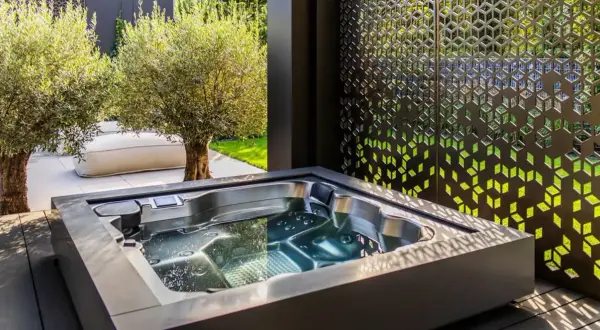 Un jacuzzi moderno en un jardín con olivos y un biombo decorativo. El lugar perfecto para un momento de relax y qué es un chill out.