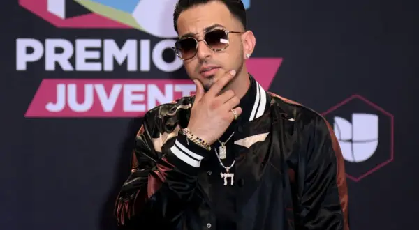 Justin Quiles poses with his hand on his chin, wearing sunglasses and a stylish jacket at Premios Juventud.
