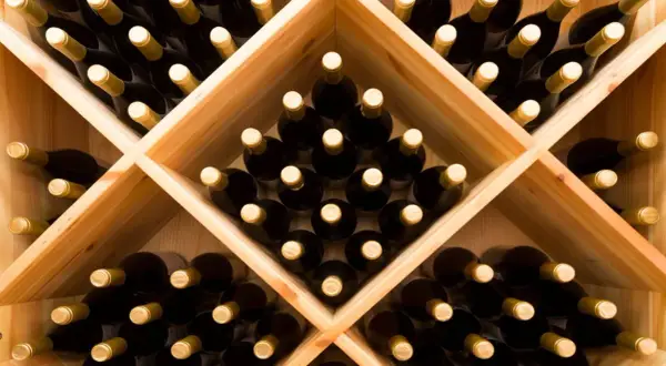 Drewniany stojak na wino wypełniony butelkami.