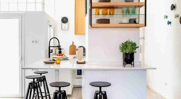 Cocinas sin muebles altos, con una isla central, taburetes negros y estanterías abiertas con vajilla.