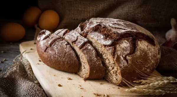 Pane di segale affettato su tagliere, con uova e spighe. Attenzione, il pane di segale fa ingrassare se consumato in eccesso.
