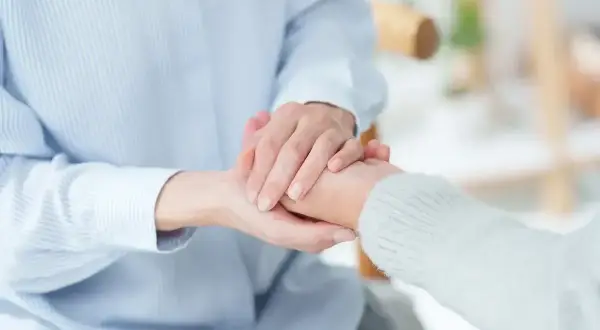 Dwie osoby trzymają się za ręce, symbolizując wsparcie. To obraz, który może kojarzyć się z pomocą finansową, np. świadczenie wspierające kwoty.