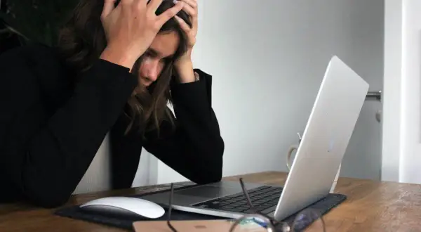 Kobieta z rękami na głowie przy laptopie, wyrażająca frustrację. To może być moment przed podjęciem decyzji o porzuceniu pracy.