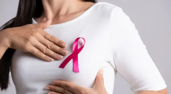 Kobieta z różową wstążką na piersi, symbolem walki z rakiem. W tle subtelne nawiązanie do leczenia, np. tamoxifen.