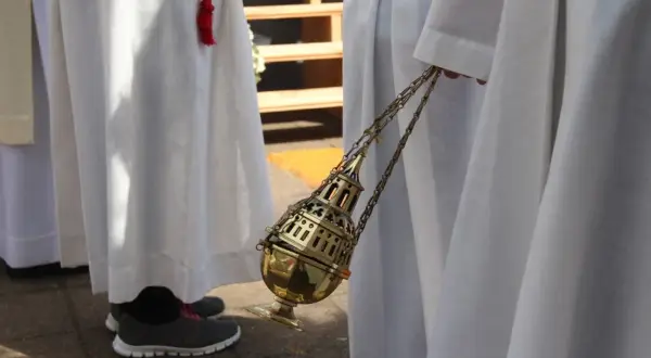 Osoba w białej szacie trzyma złote kadzidło na łańcuszku.
