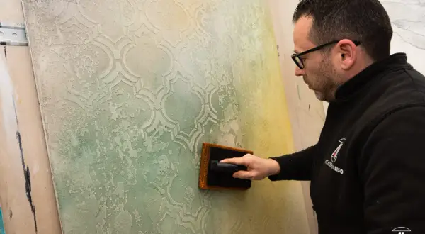 Un artigiano applica pittura per marmo su una parete con un motivo a rombi, creando un effetto materico e anticato.