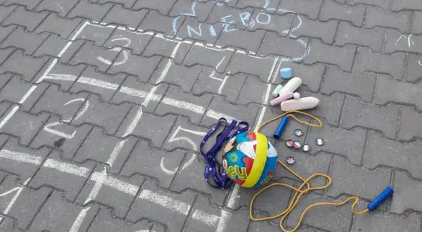 Kreda rysuje podwórkowe zabawy z piłką, skakanką i kredą. Chmurka z napisem "NIEBO" zaprasza do gry.