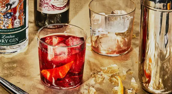 Zutaten für einen Negroni: Gin, roter Wermut und Campari. Serviert mit Eis und Orangenzeste.