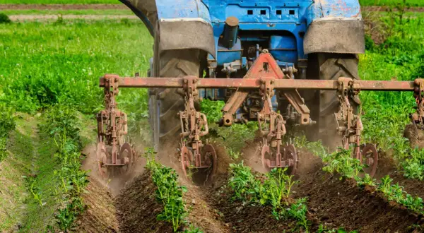 Niebieski traktor z narzędziami uprawia pole, wspierając rolnictwo regeneratywne.